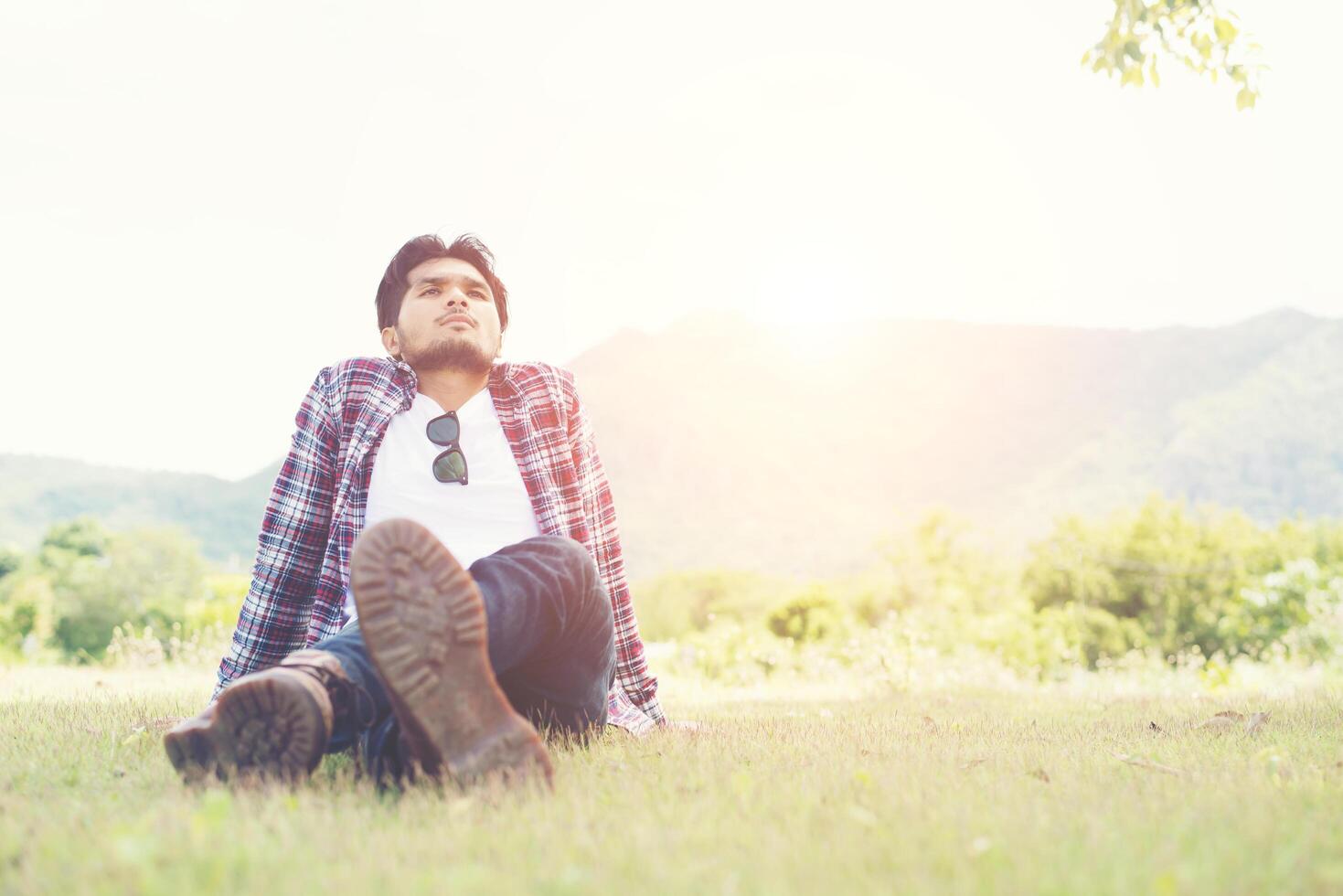 joven hipster sentado en el césped del parque, disfruta del aire natural y fresco. foto