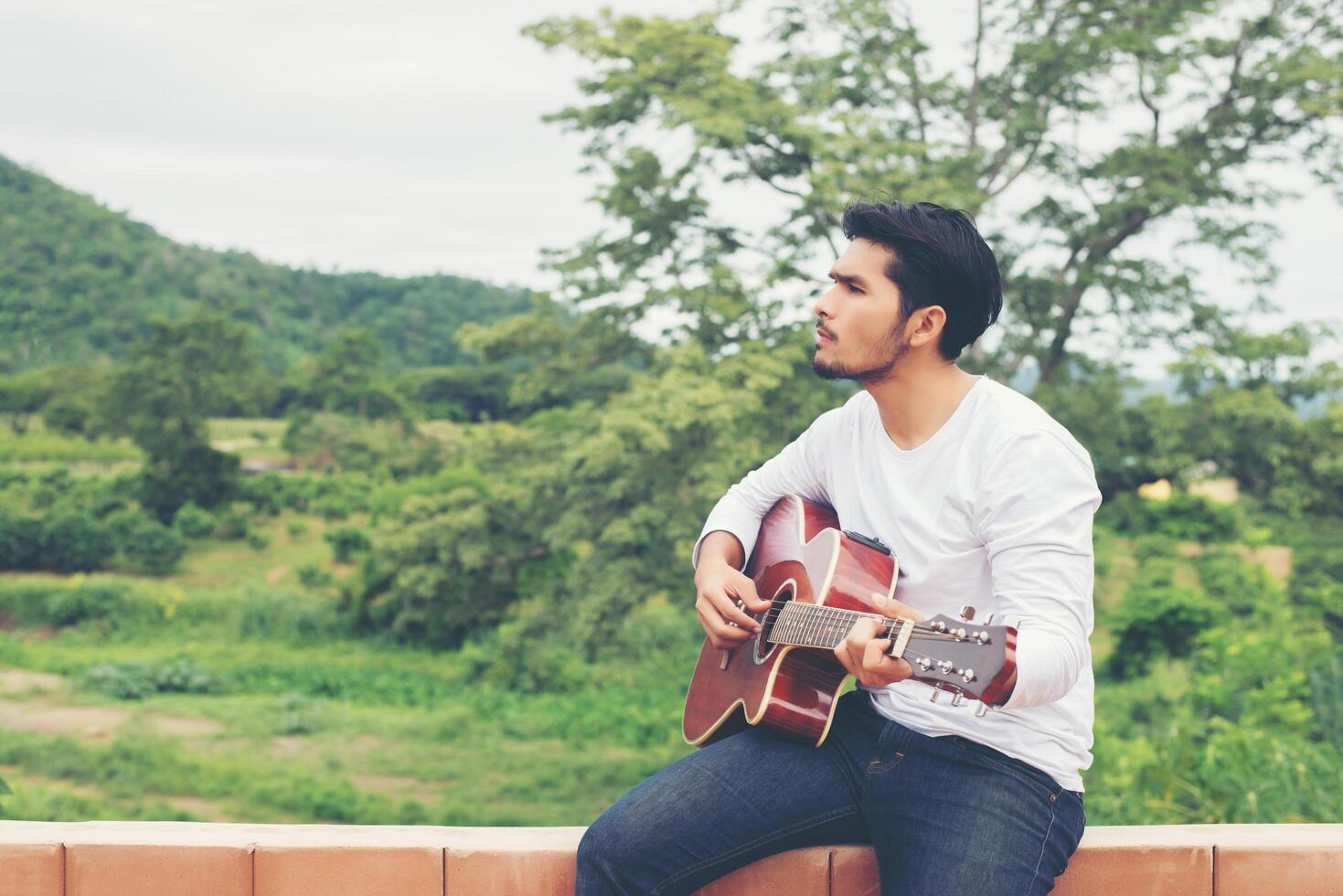 Young hipster man playing guitar to relaxing on his holiday, enjoy with natural and fresh air. photo