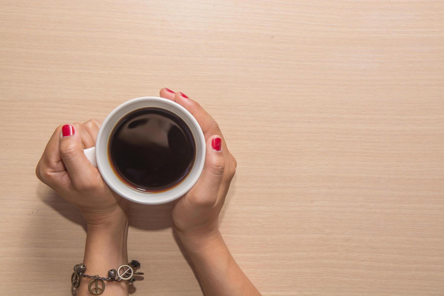 Woman's hands hold a cup of coffee on wooden table. photo