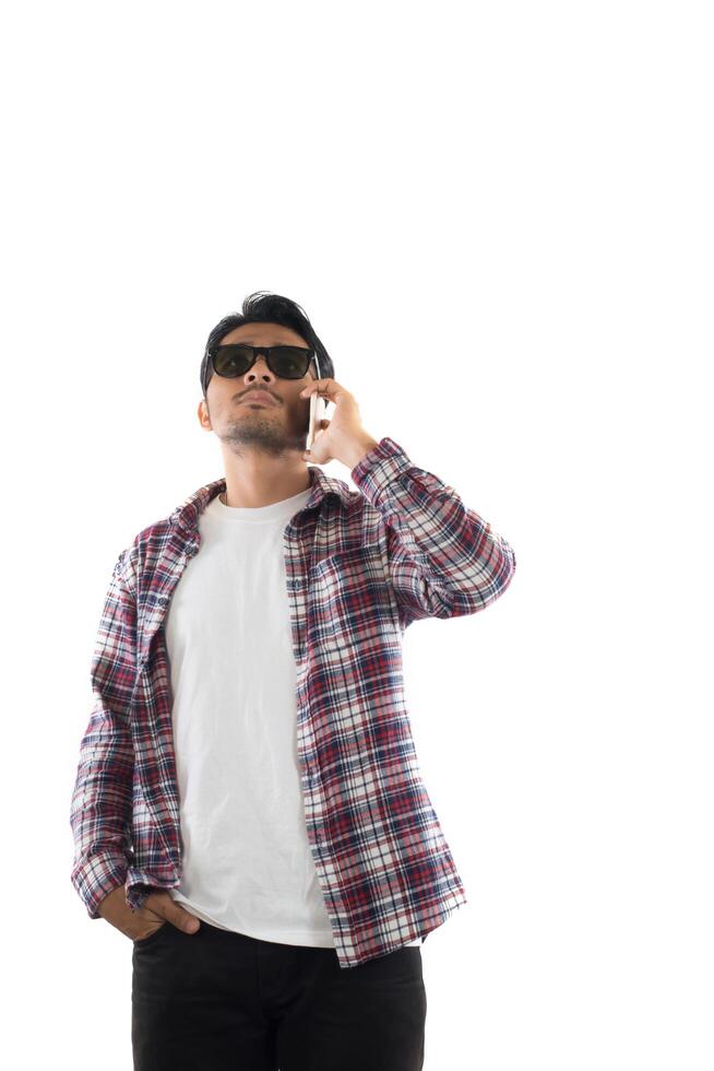 Handsome hipster young man in hat and sunglasses standing and talking on mobile phone over white background. photo