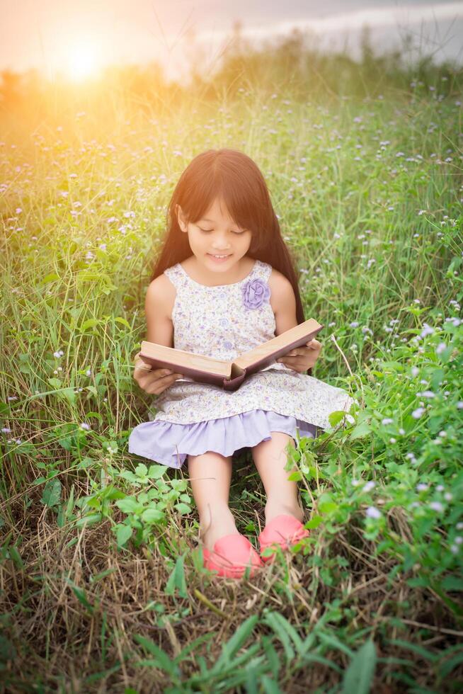 linda niña asiática leyendo un libro en la naturaleza. foto