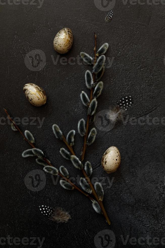 Happy Easter concept. Preparation for holiday. Golden decorated easter eggs willow feather on trendy grunge scratched dark black shale background. Simple minimalism flat lay top view, copy space photo