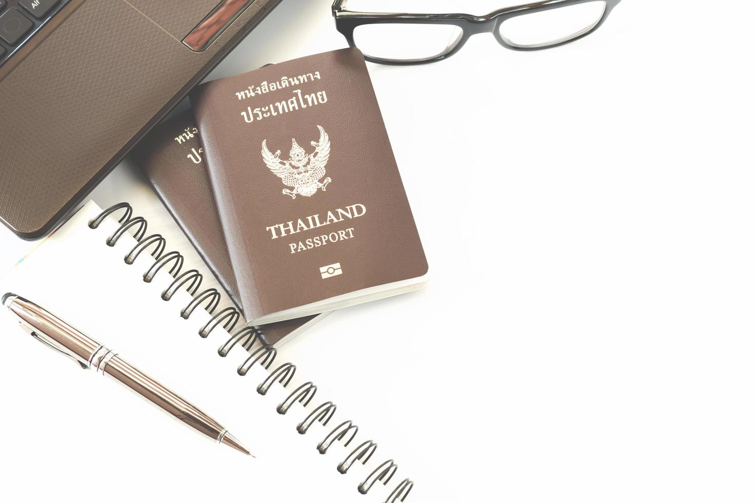 accesorios de viaje disfraces. pasaportes de tailandia, preparación para viajar, bolígrafo en la parte superior, anteojos y computadora portátil o computadora para el tiempo de vacaciones, enfoque suave. foto