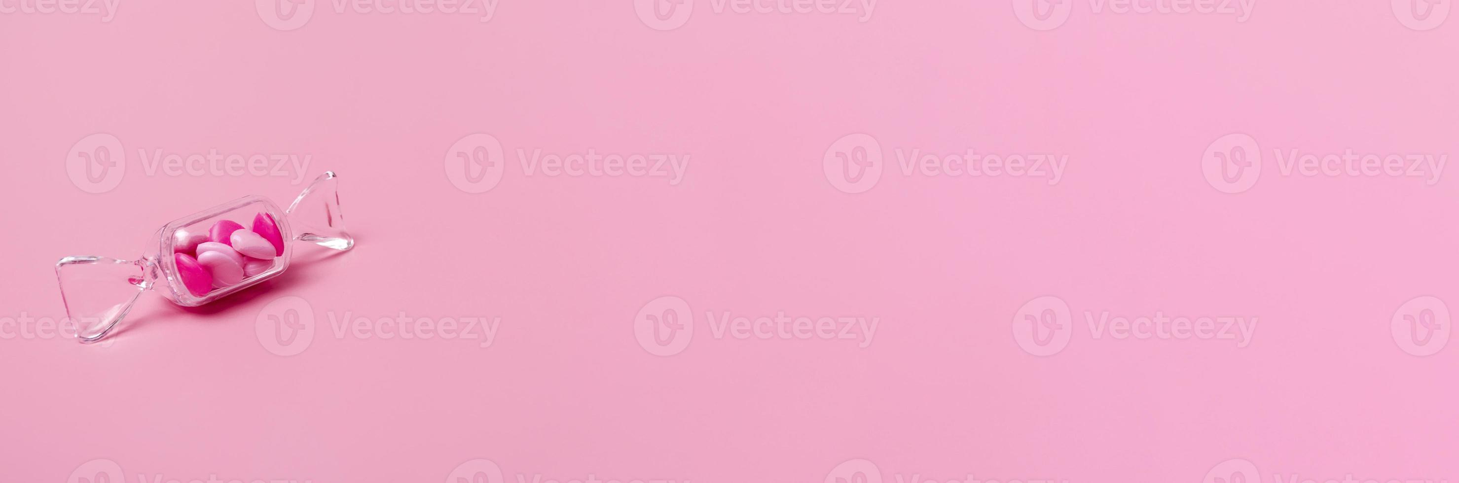 Transparent box in the shape of a candy with sweet heart lollipops on a pink background copy space. Banner photo