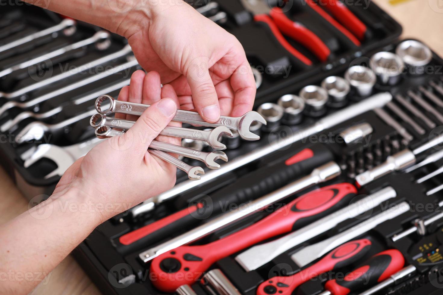 Tool store. Closeup of male hand holding wrenches. Auto repair kit in toolbox. Repairman instruments set. Inside the toolbox there are black-red wrenches, spanners and different nozzles. Closeup. photo