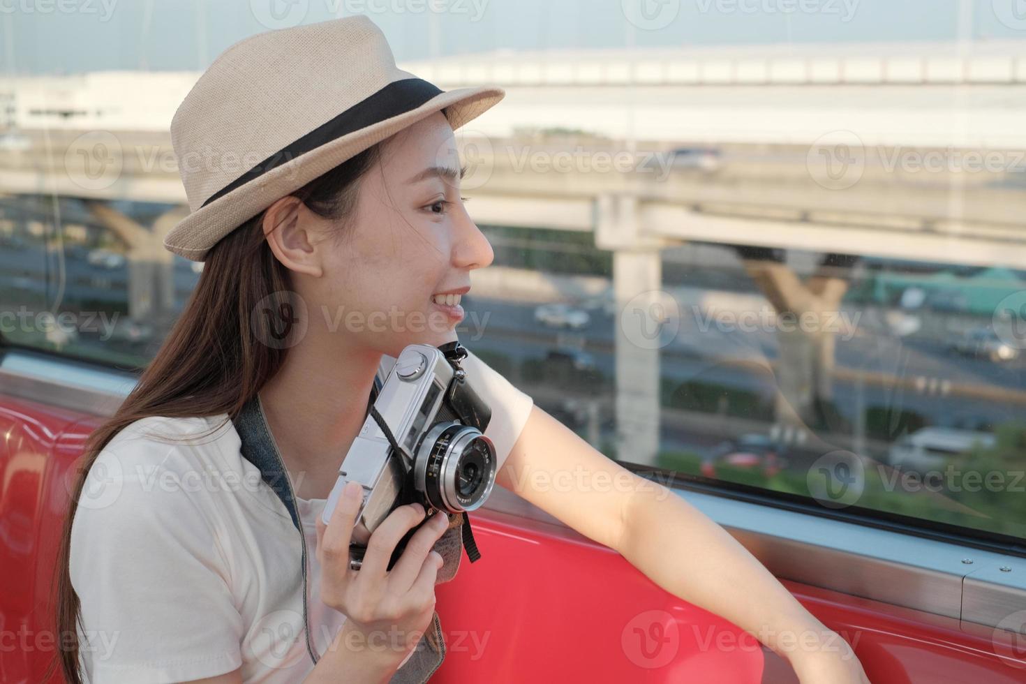 una hermosa turista asiática se sienta en un asiento rojo, viaja en tren, toma una foto instantánea, se transporta a la vista de los suburbios, disfruta del estilo de vida de los pasajeros en tren, feliz viaje de vacaciones.