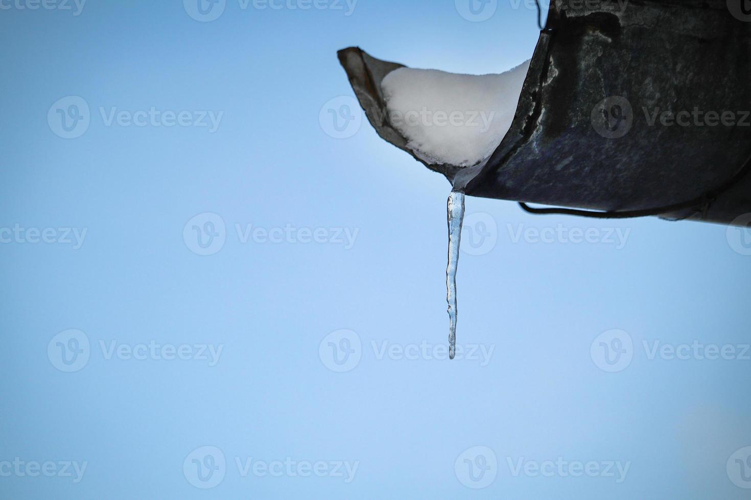 Small icicle hanging on draining roof pipe edge photo