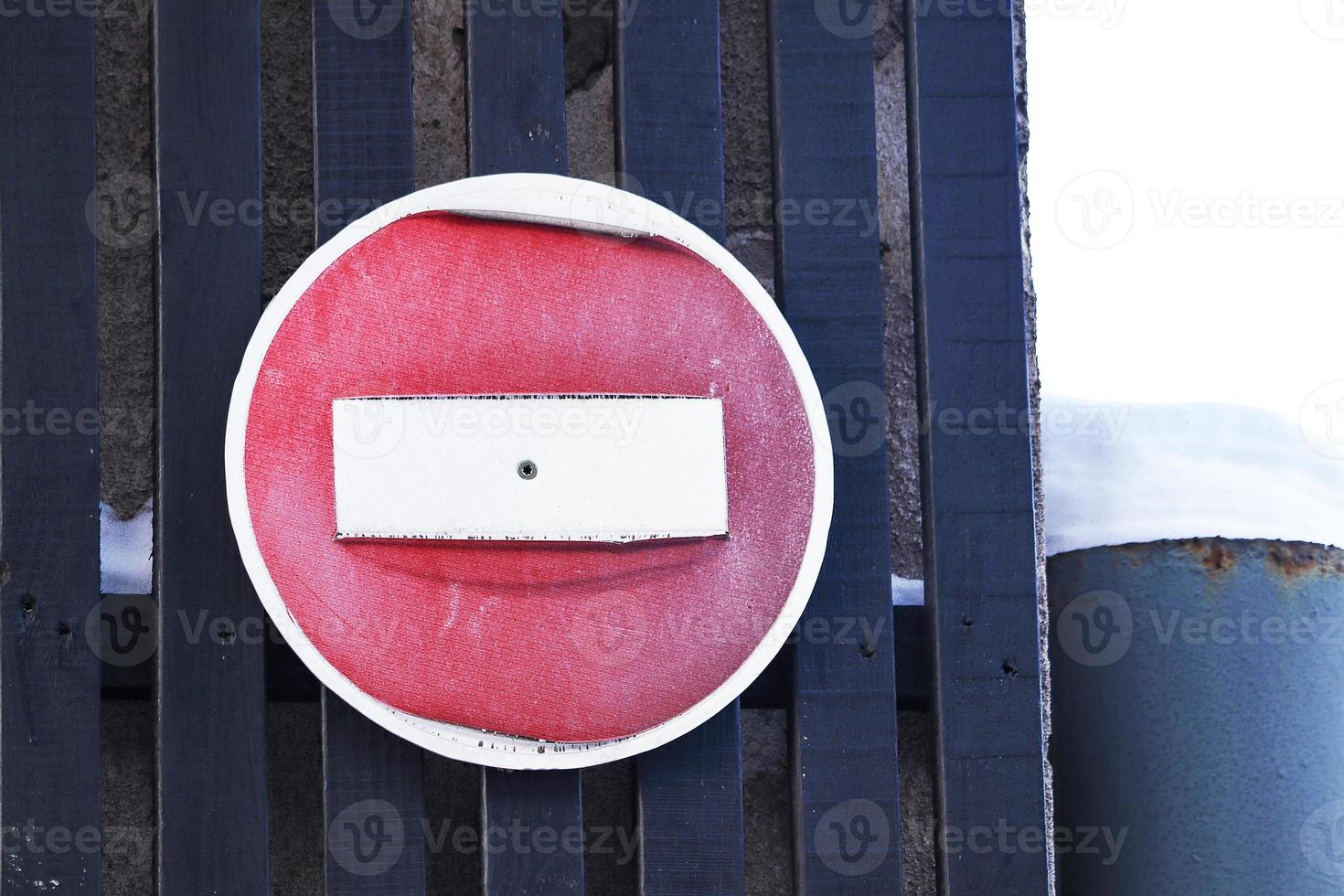 Old weathered red stop road sign hanging onblack planks fene near huge snow on column photo