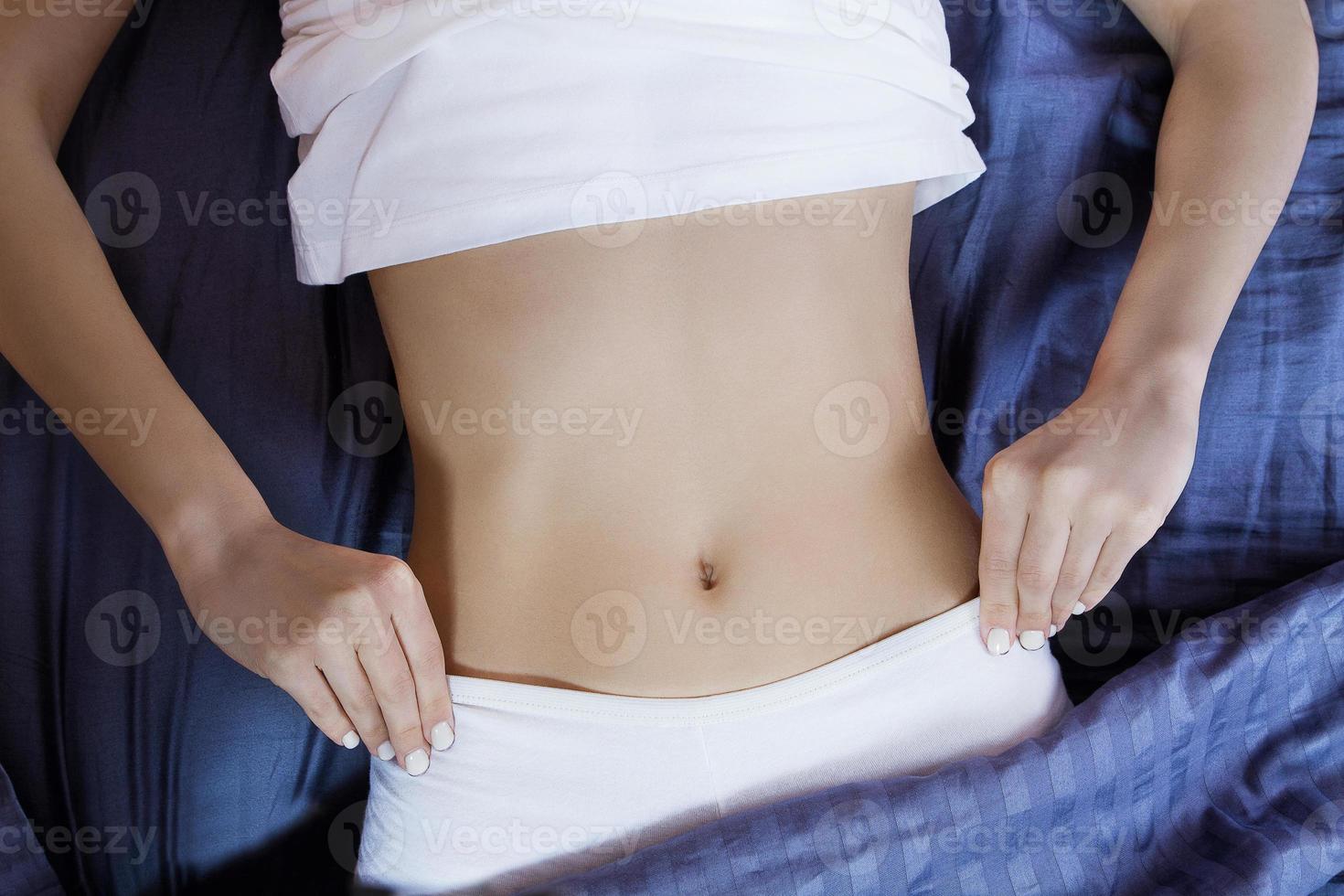 Healthy nutrition and belly health concept. Close up of woman flat stomach. Girl in bed with hungry feeling. Top view. Banner photo