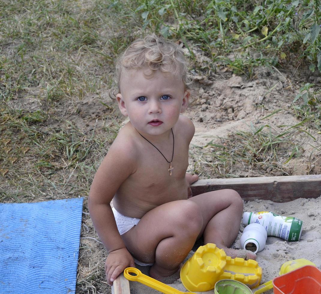 Beautiful baby in child sandpit posing photographer near sandbox photo