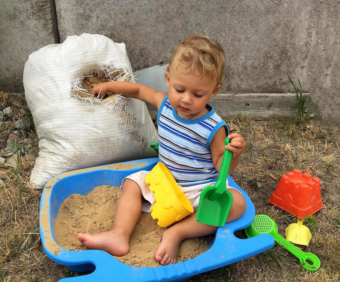 Beautiful baby in child sandpit posing photographer near sandbox photo