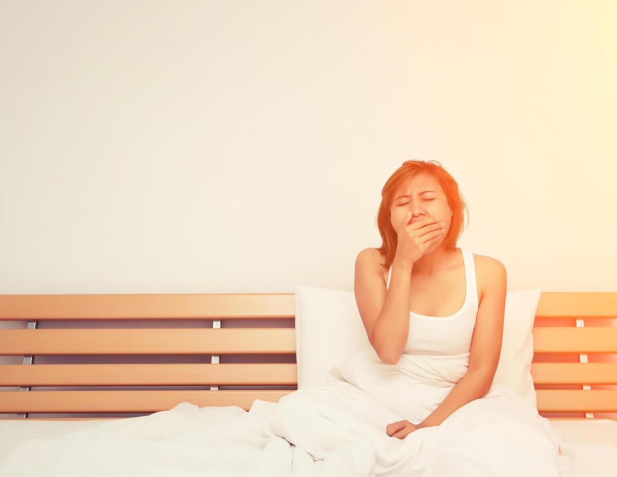 beautiful young woman sitting on the bed and yawning when she wake up in the morning photo