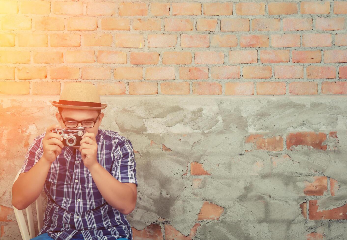 Hipster handsome man take a photo by retro camera on the brick background