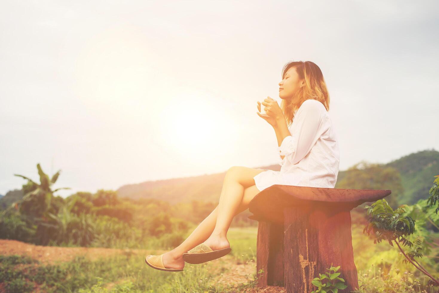 Beautiful young woman holding up a cup of coffee sitting on the bench a fresh breeze in the morning. photo