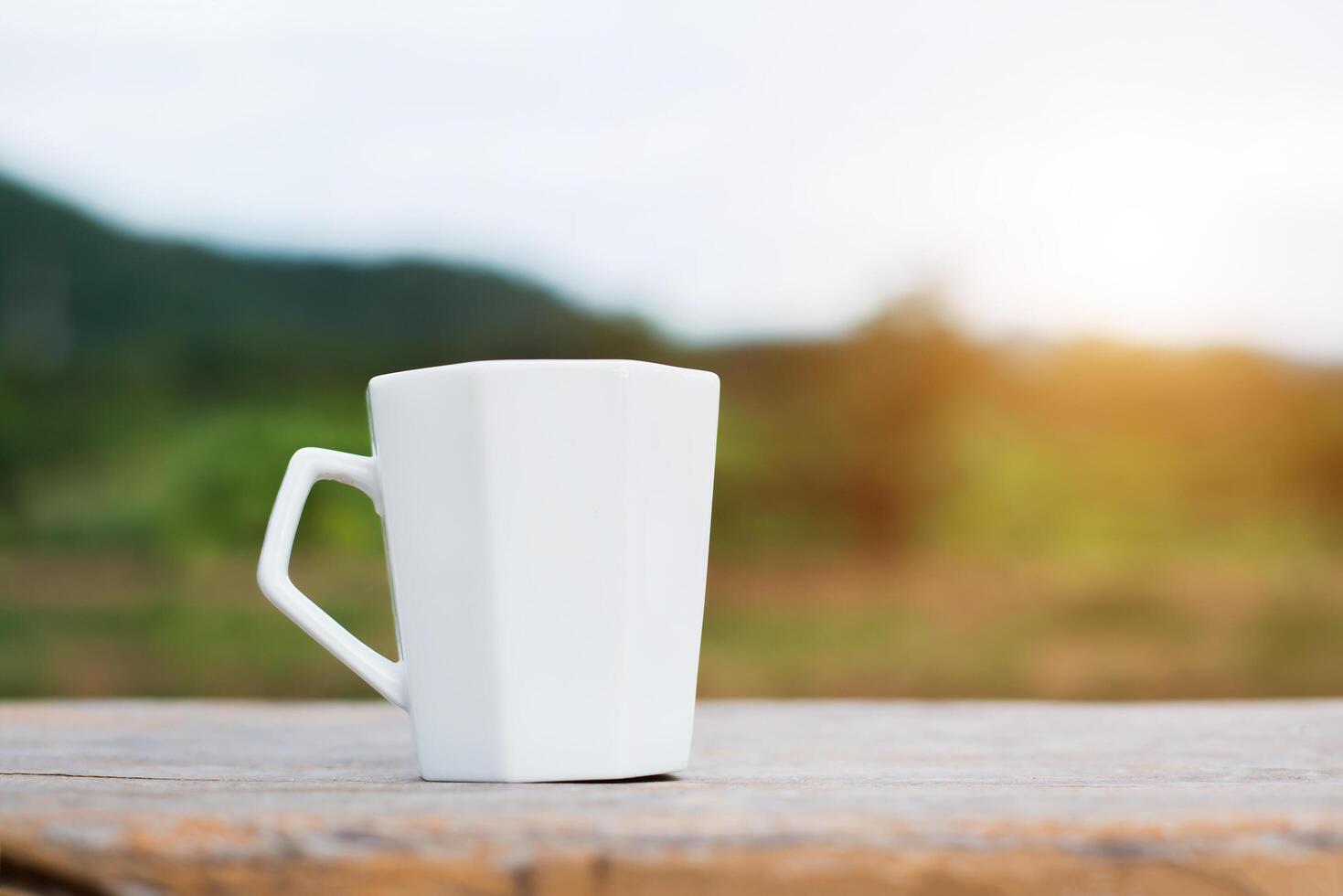 White cup of hot coffee on mountain natural green background. photo