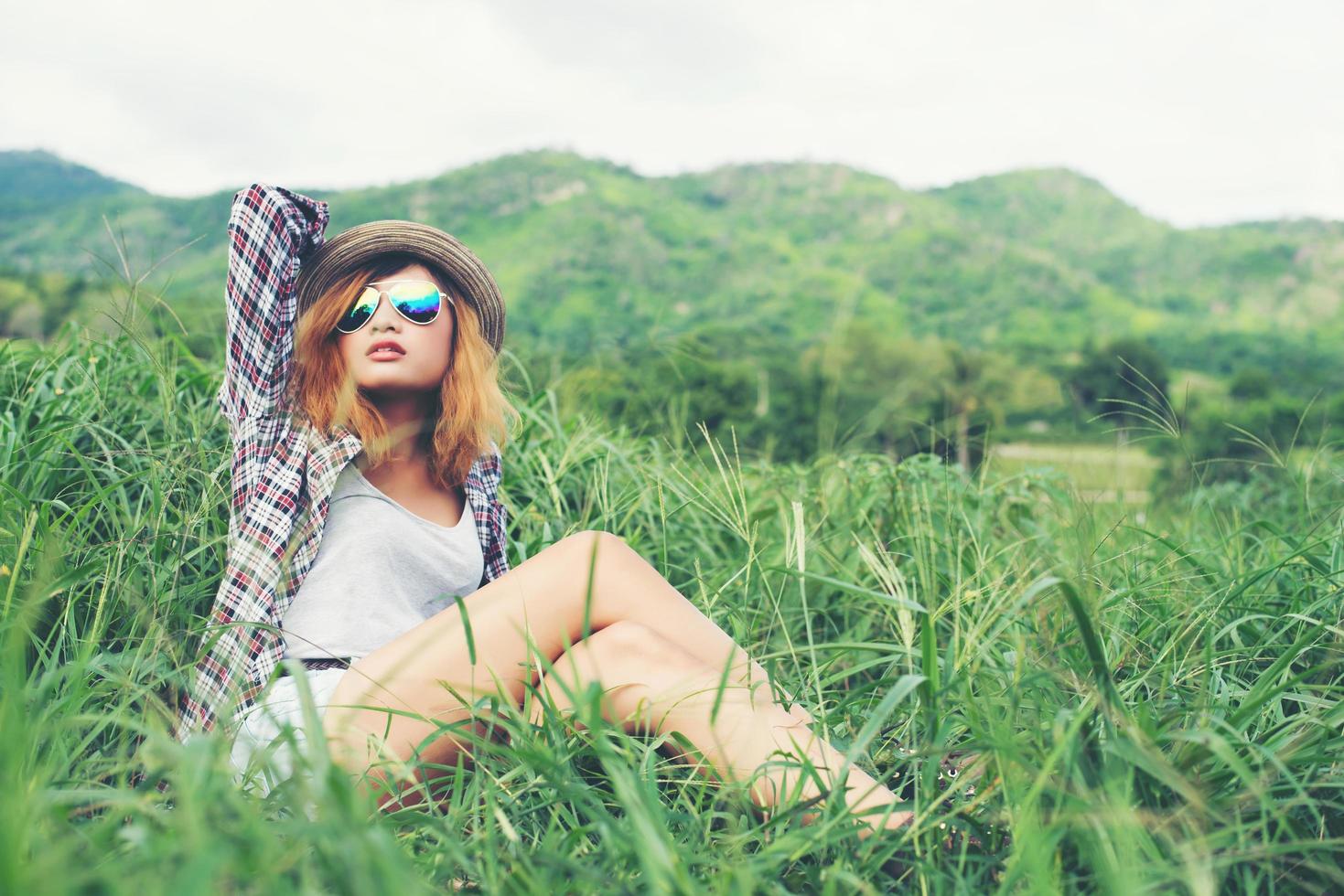 hermosa mujer hipster sentada en un prado con naturaleza y montañas al fondo. foto