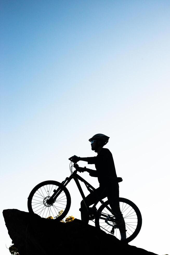 Silhouette of the athlete standing on the rock with bicycle photo