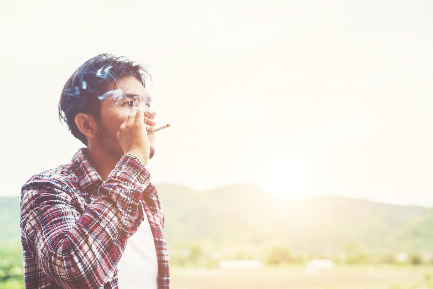 Hipster man smoking cigarette, standing behind a mountain. Among the fresh air in the morning. photo