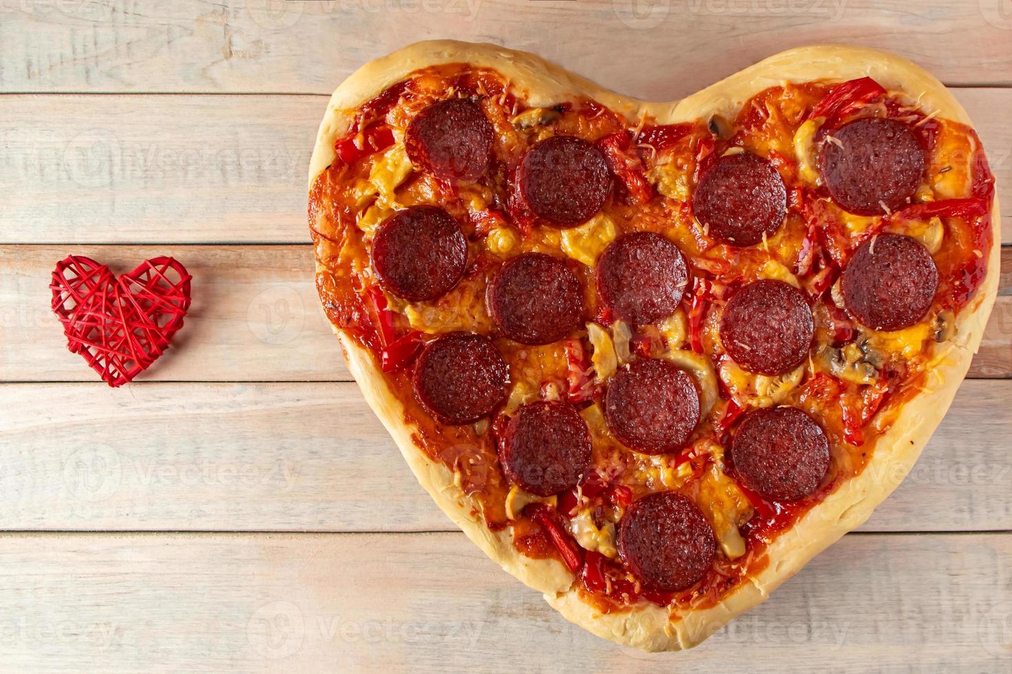 Heart shaped pepperoni pizza on wooden background. Valentines day gift. photo