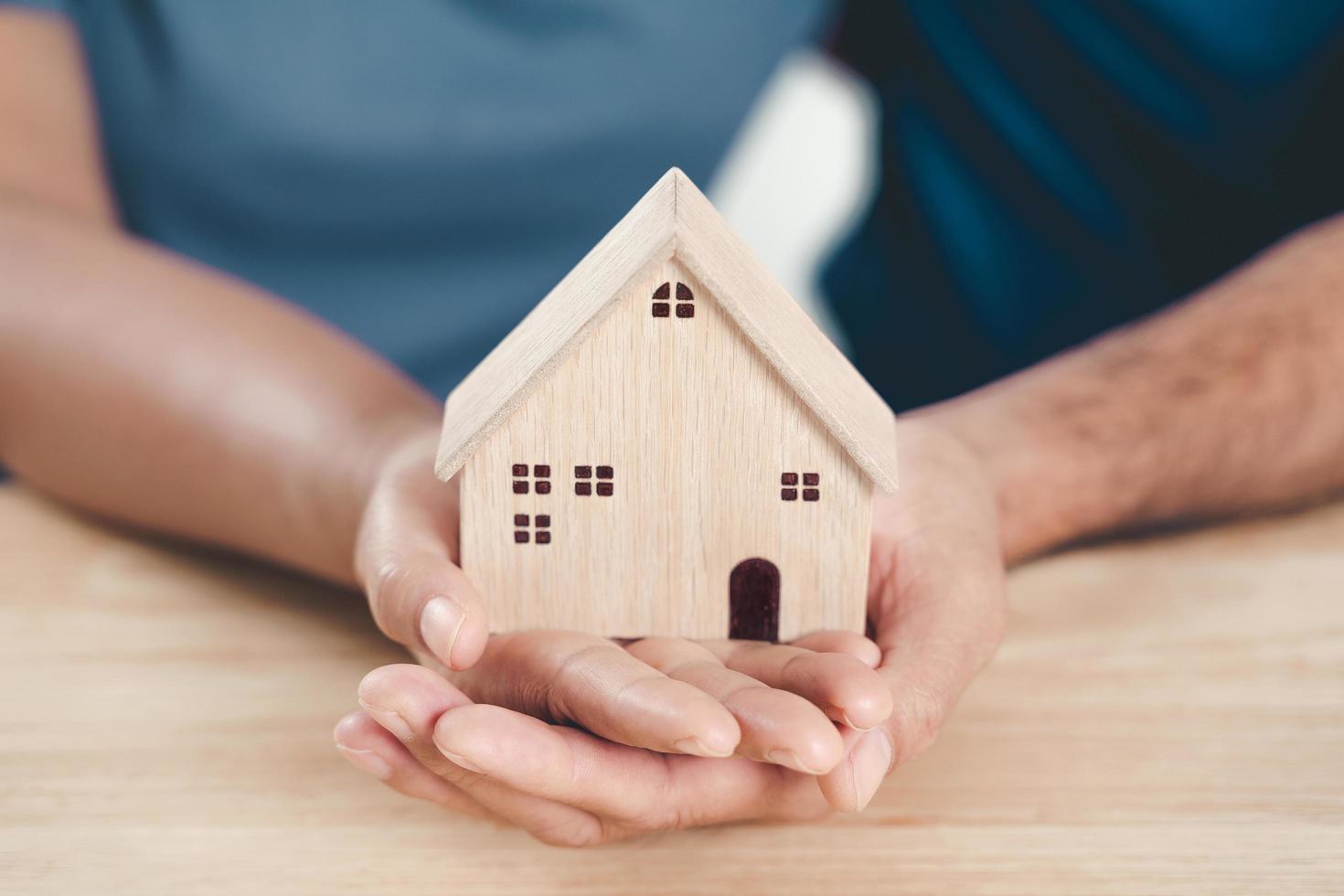 Man husband and Woman wife hands holding wooden house on the wood table background. family home, foster care, homeless charity support concept, financial plan home loan concept. photo