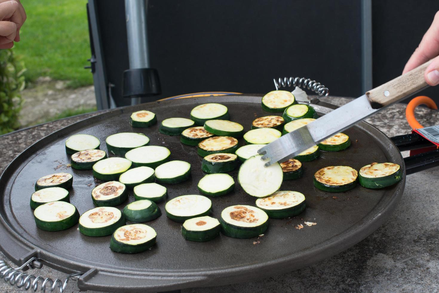 Preparing sliced zucchini on a grill. Hand moving the slices with tongs photo