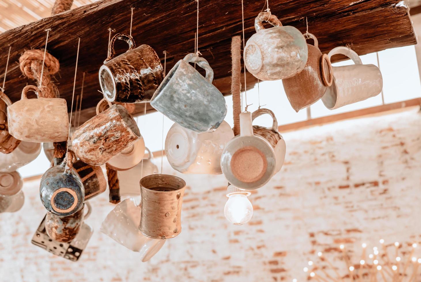 Collection of Clay pottery Cups hanging with the ropes from ceiling in coffee shop photo