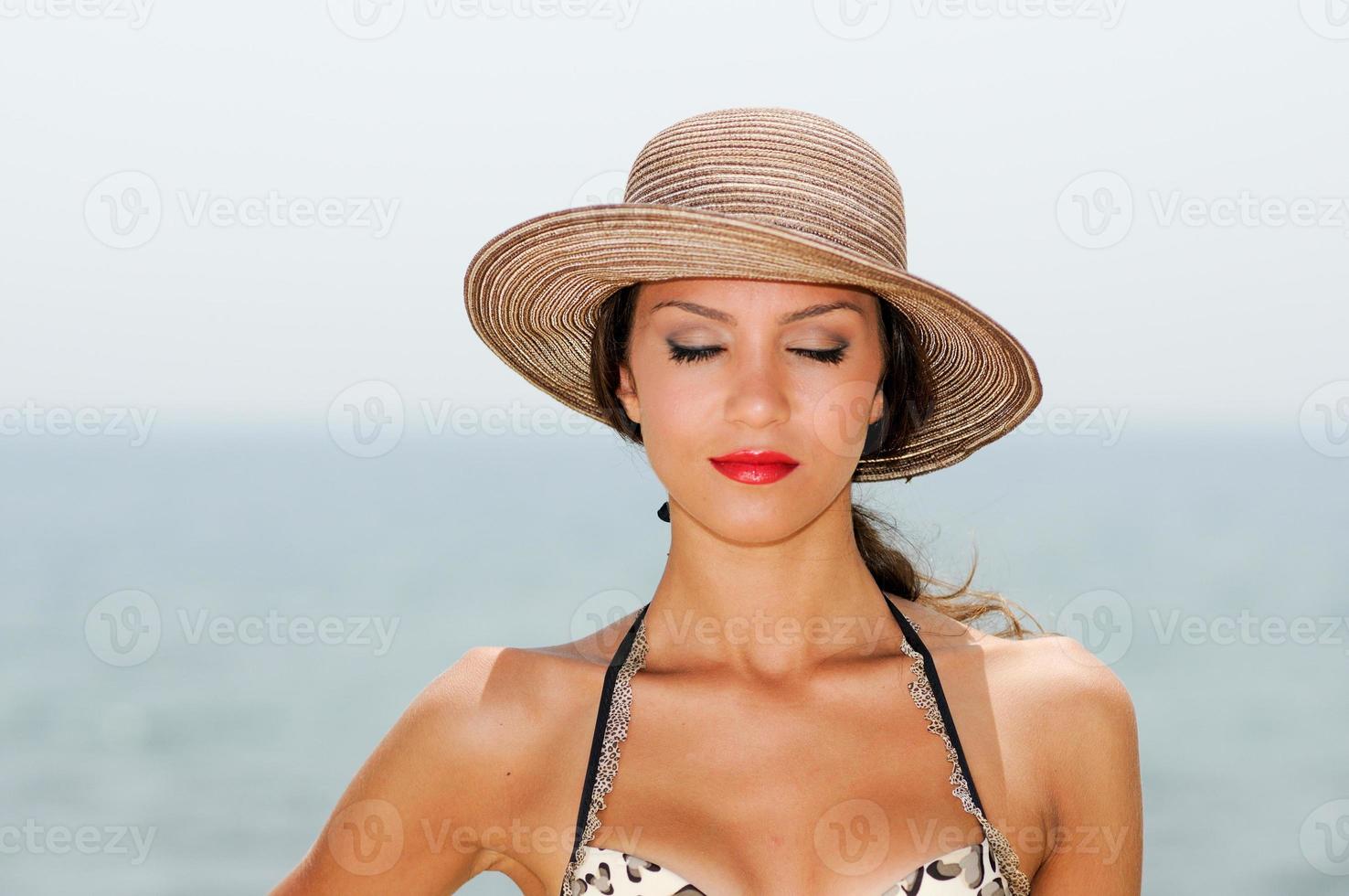 Attractive woman with a sun hat on a tropical beach, eyes closed photo