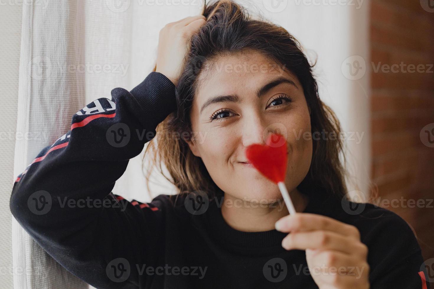 Latin woman in love with a lollipop in her hand in the shape of a heart. Valentine's Day photo