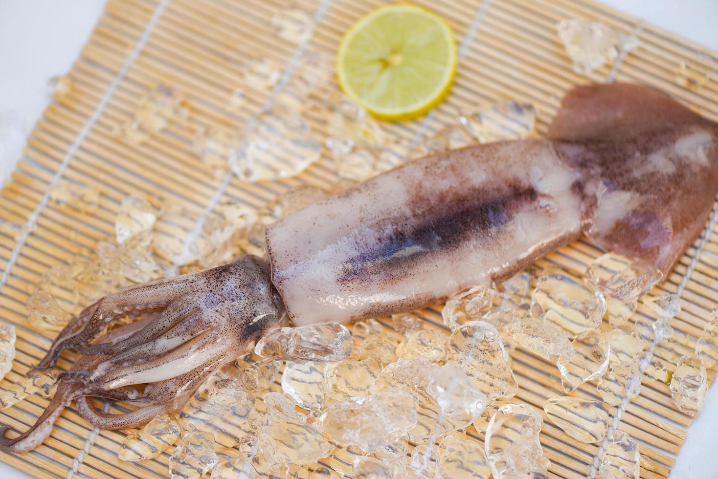 calamares frescos, pulpo o sepia para comida cocinada en el restaurante o en el mercado de mariscos, calamares crudos sobre hielo con especias de ensalada, lima limón en el fondo de madera foto