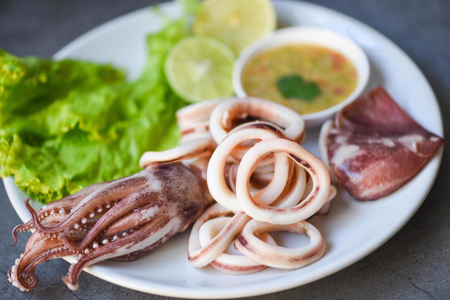 Fresh squid cooked boiled with lettuce vegetable salad lemon and seafood sauce on table background, squid rings on white plate photo