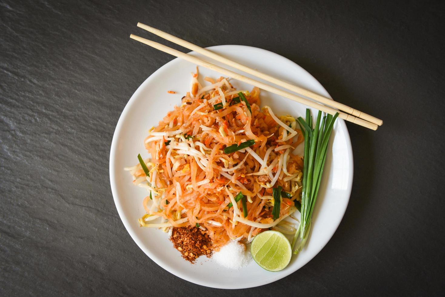 Thai food fried noodle Thai style with prawns bean sprout and garnish peanuts chili powder sugar lemon lime, Stir-fry noodle Pad Thai on plate served on the dining table food - top view photo