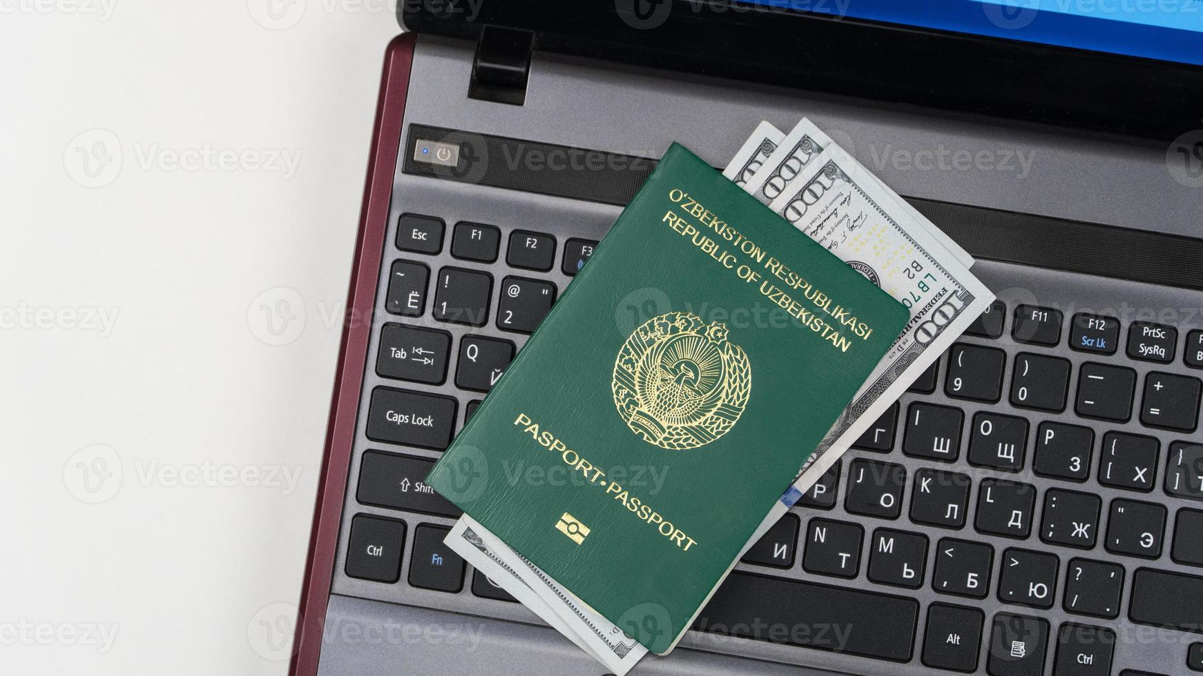 pasaporte de uzbekistán con dólares estadounidenses en el teclado de la computadora portátil. Registro en línea. concepto - soborno y corrupción. vista superior foto