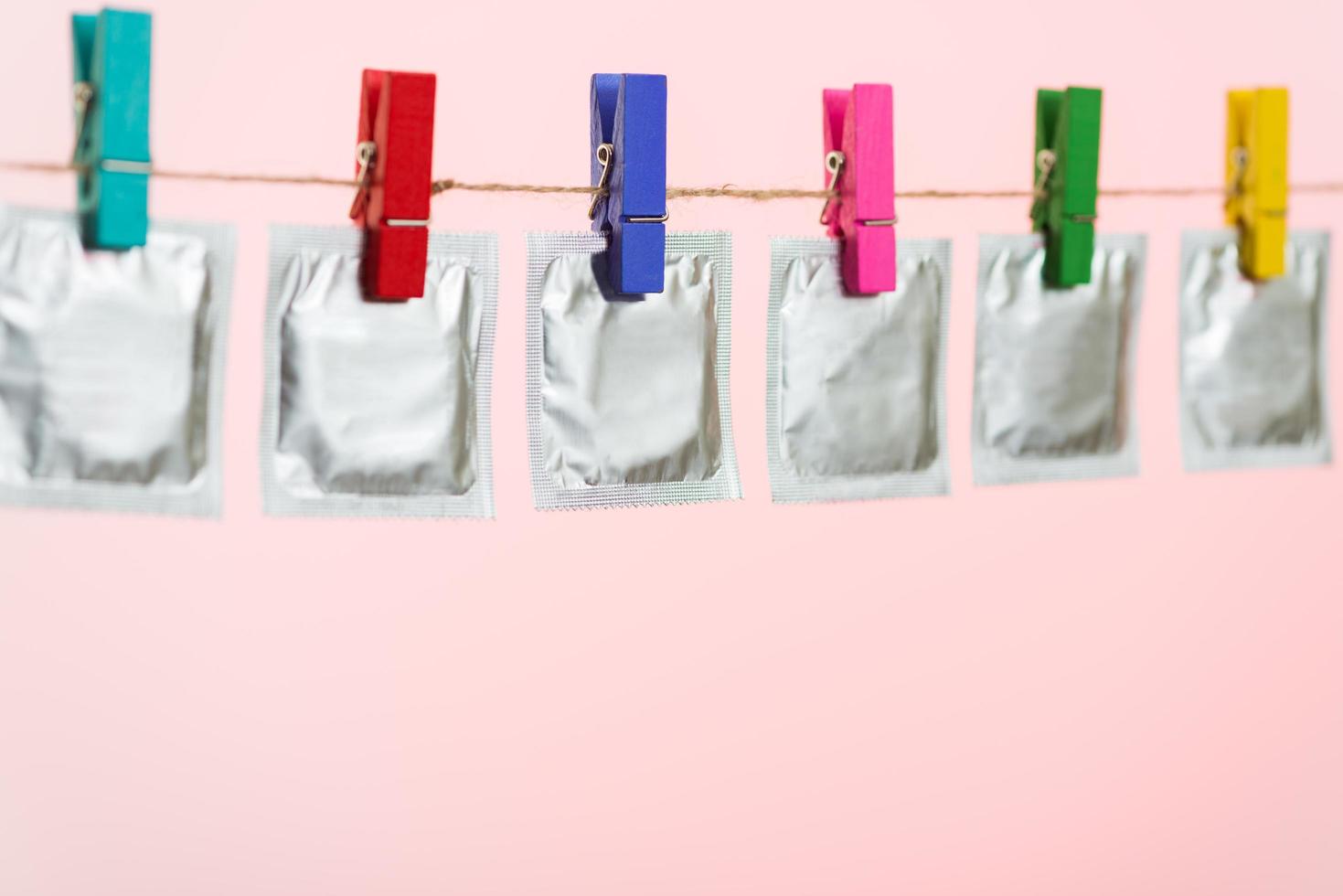 Condoms hanging on the rope on light pink background. photo