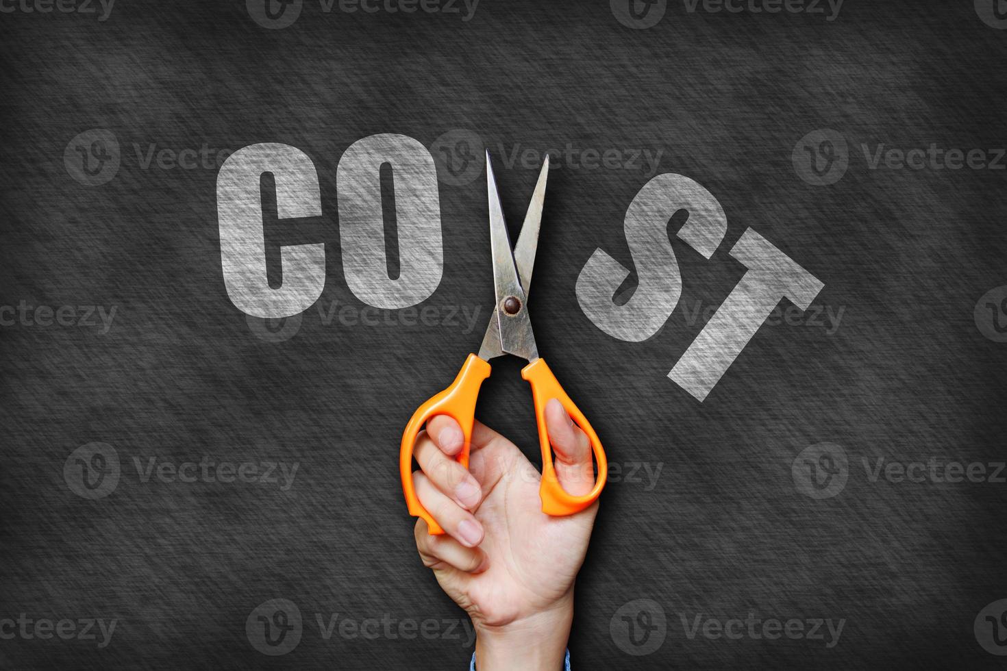 Businessman holding scissor cutting cost text on blackboard background. photo