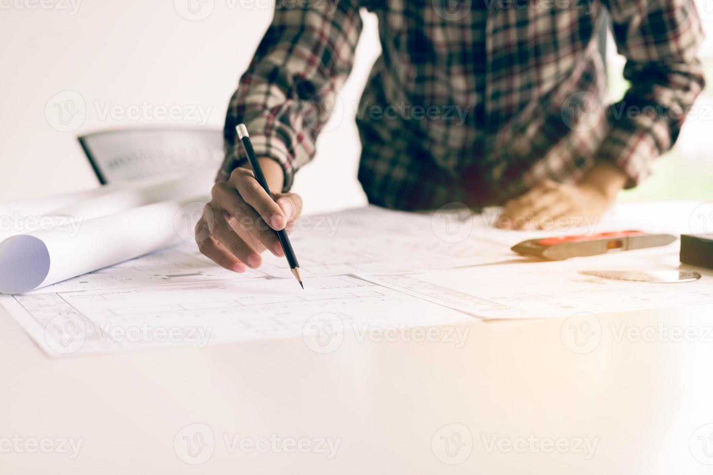 Hand of young engineering man drawing on blueprint at table in office room. photo