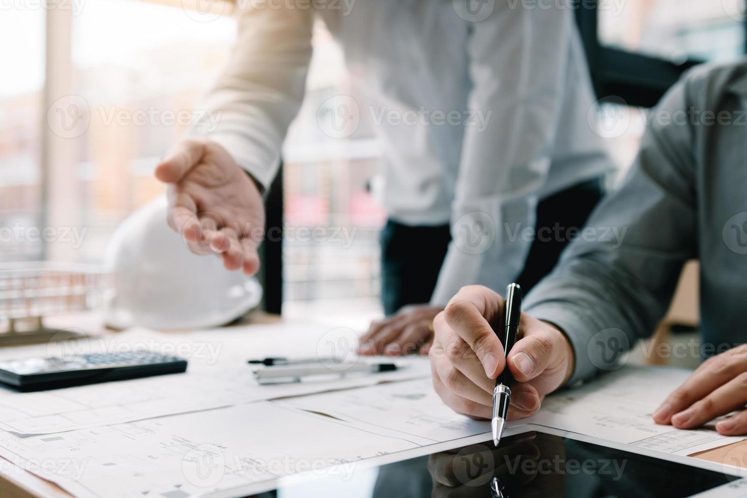 Two engineering working together and using digital tablet looking blueprint and analysis with architectural plan on desk. photo