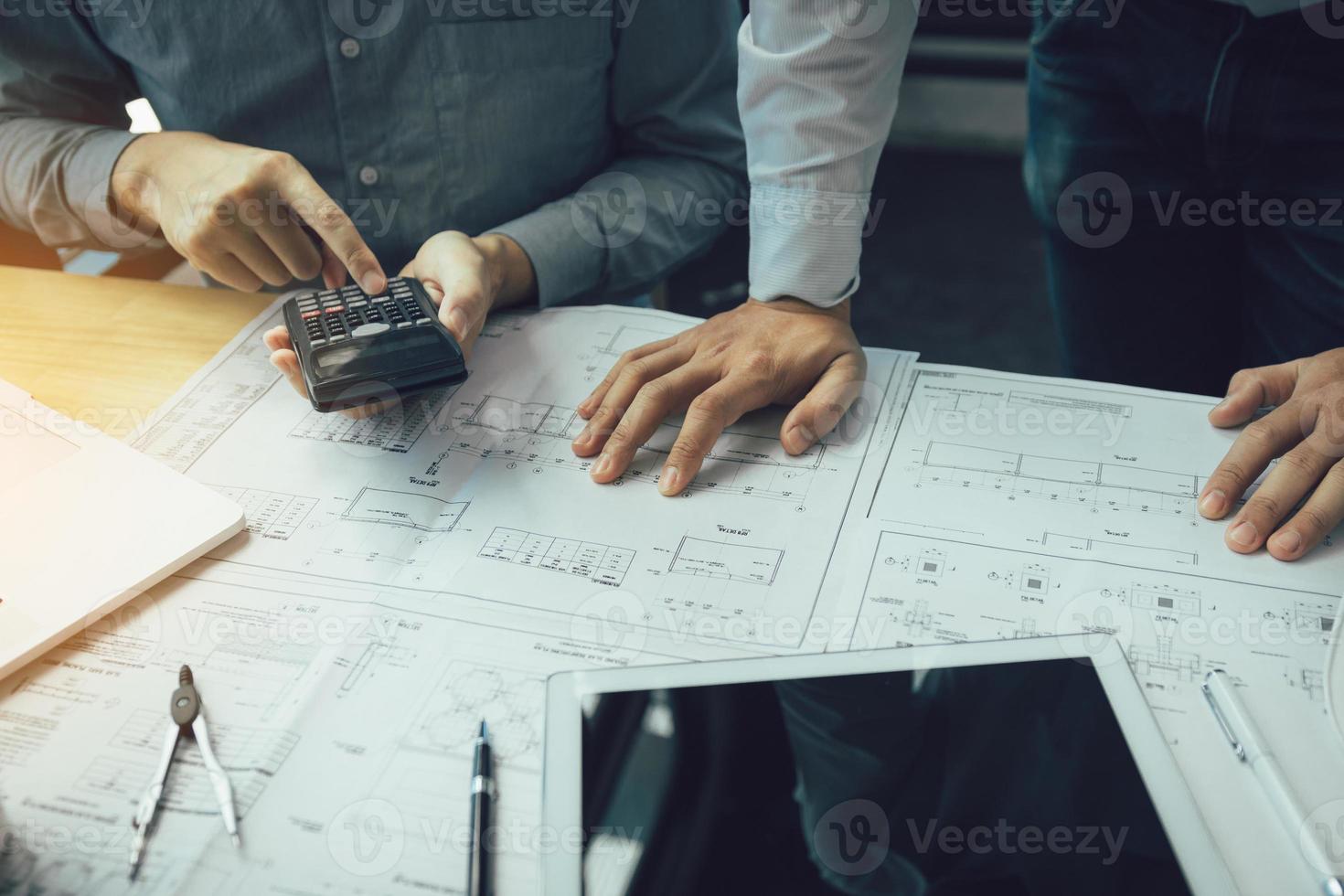 Two engineering working together and using digital tablet looking blueprint and analysis with architectural plan on desk. photo