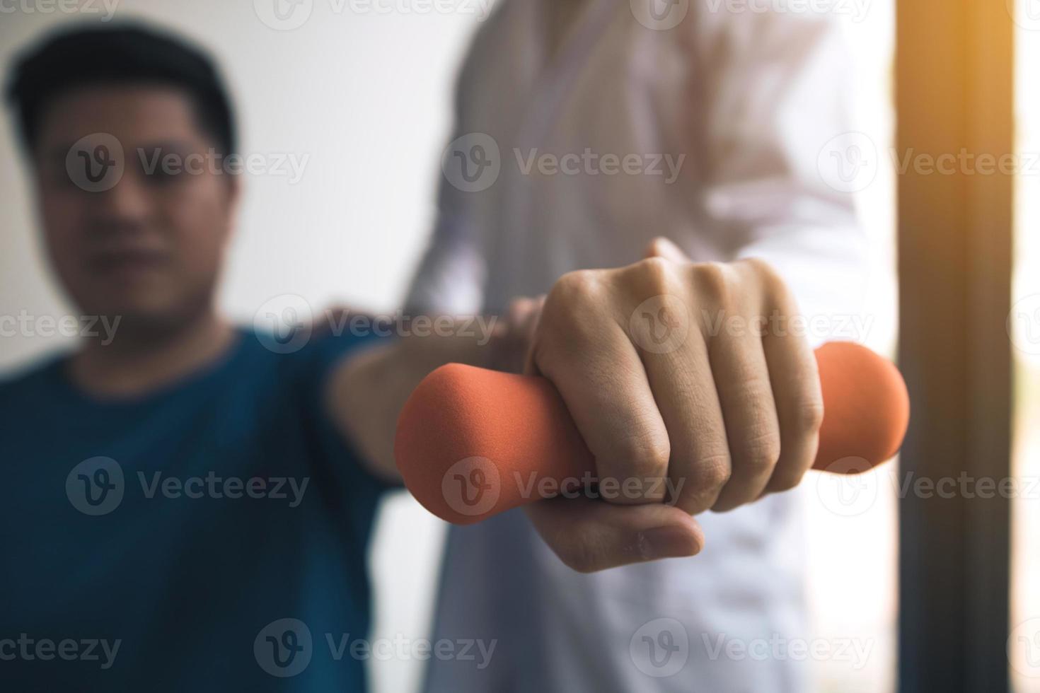 Asian physiotherapist helping a patient lifting dumbbells work through his recovery with weights in clinic room. photo