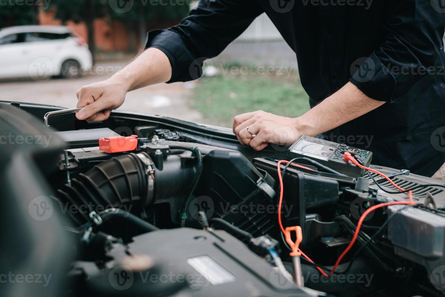 Car mechanic is checking the engine and holding the battery gauge. photo