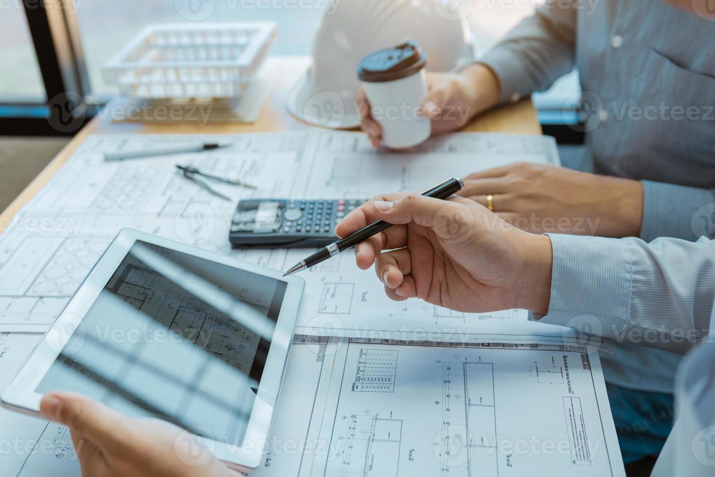 Two engineering working together and using digital tablet looking blueprint and analysis with architectural plan on desk. photo