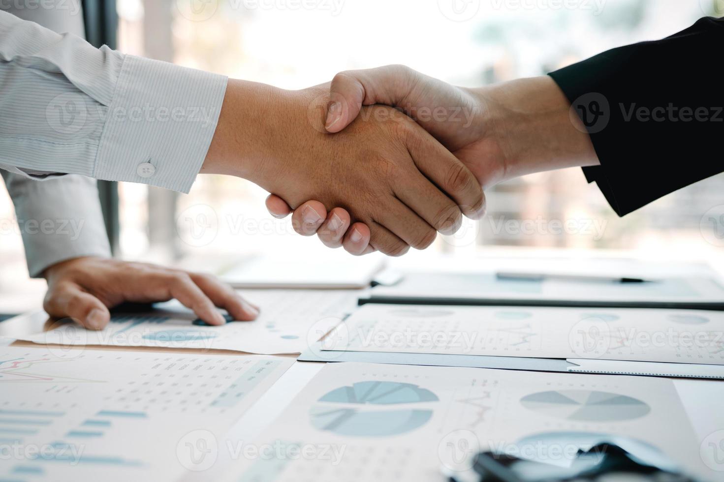 Entrepreneurs collaboration deal shaking hands in a modern office and financial paper graph on desk. photo