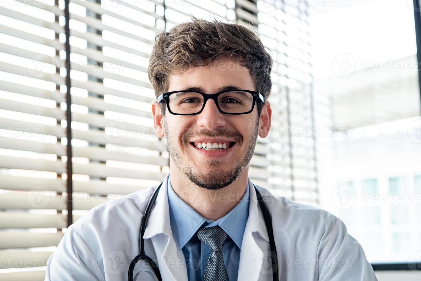 doctor joven feliz sonriendo a la cámara mientras hace videollamadas en línea, conceptos de servicio de consulta médica en el hogar foto