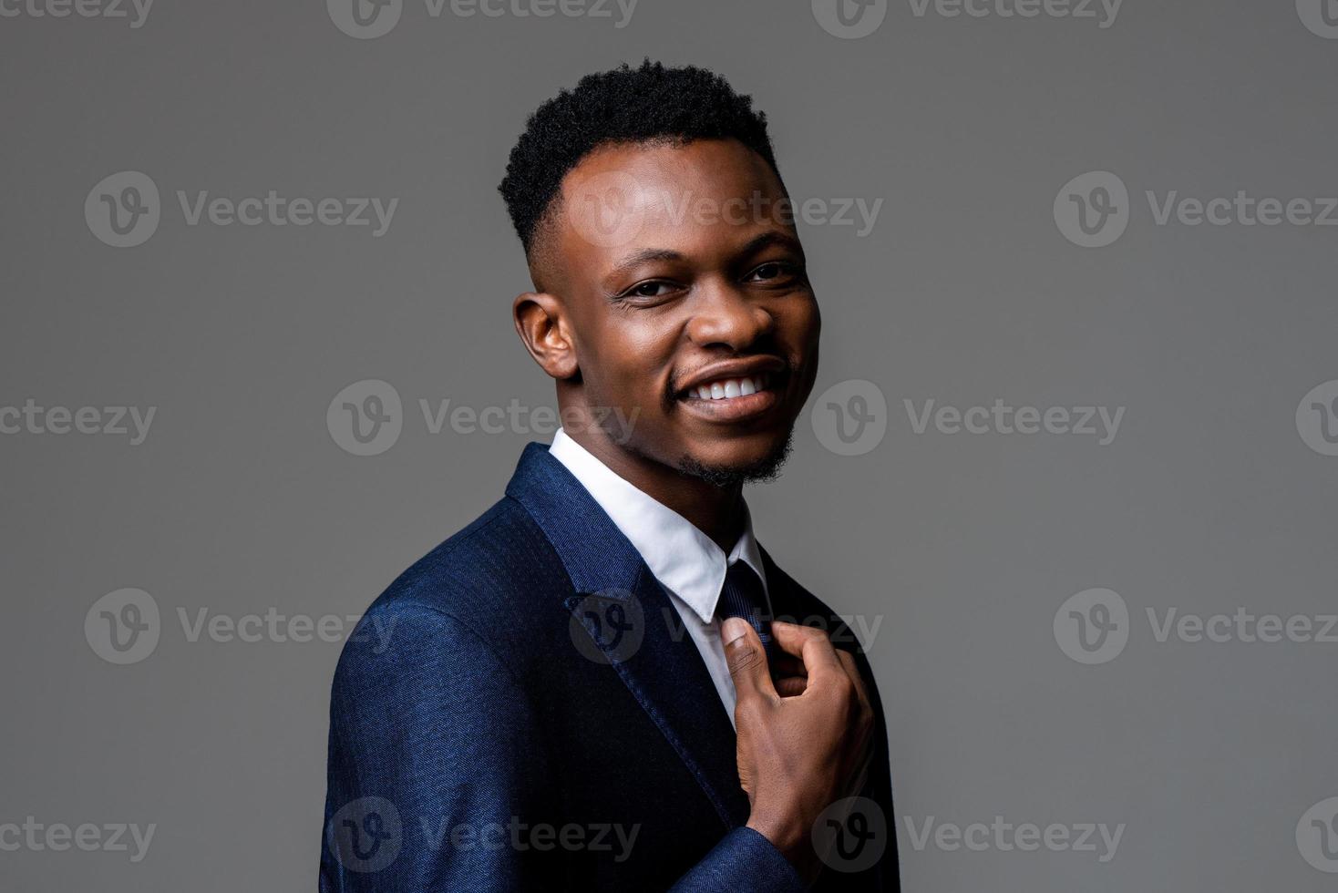 joven sonriente alegre y apuesto hombre africano con traje de negocios formal en un estudio de fondo gris aislado foto