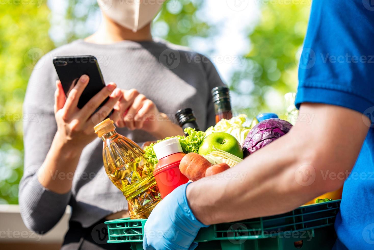 Woman customer wearing face mask checking grocery that ordered online and delivered by deliveryman at home, food delivery service in the times of COVID-19 concept photo