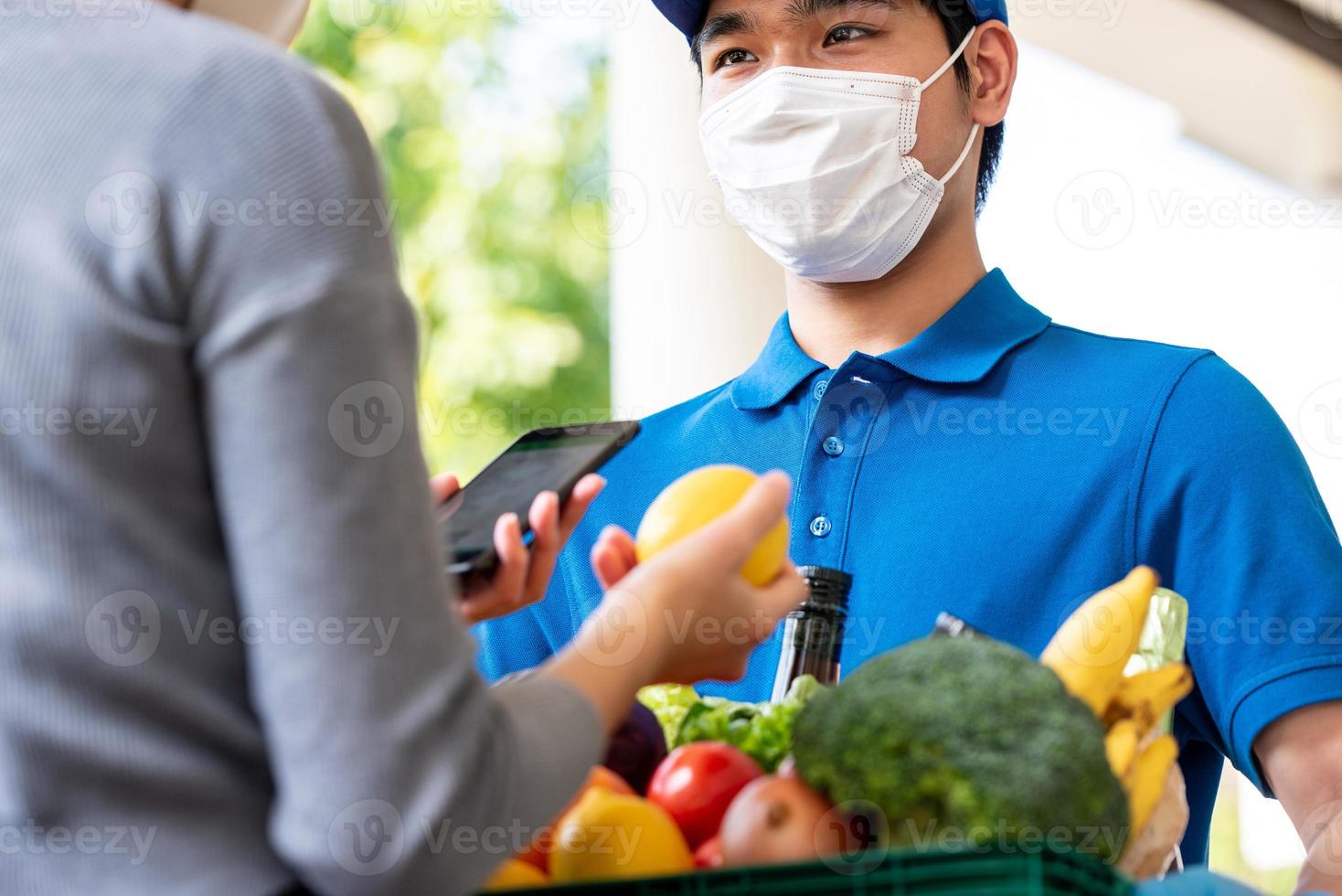 Hygienic Asian deliveryman wearing face mask while delivering groceries to customer at home,  food delivery in the time of pandemic concept photo