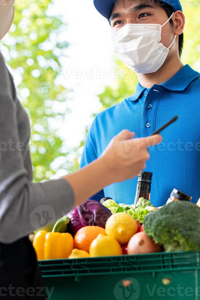 Asian deliveryman wearing face mask while delivering groceries to customer at home, food delivery service in the time of pandemic concept photo