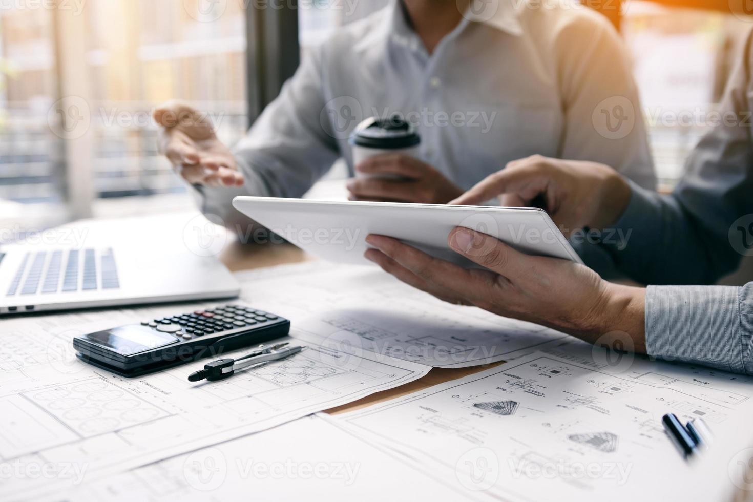 Two engineering working together and using digital tablet looking blueprint and analysis with architectural plan on desk. photo