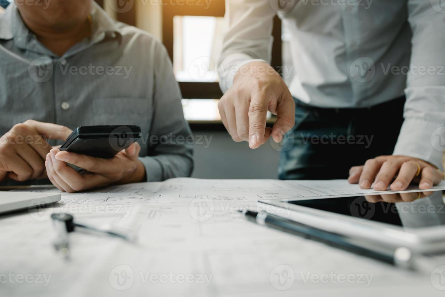 Two engineering working together and using digital tablet looking blueprint and analysis with architectural plan on desk. photo