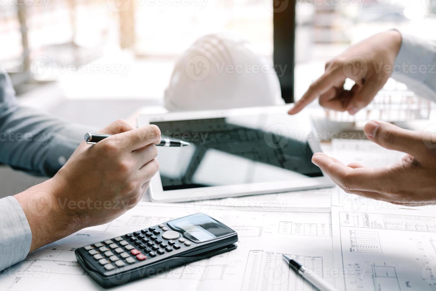 dos ingenieros trabajando juntos y usando una tableta digital buscando planos y análisis con un plan arquitectónico en el escritorio. foto