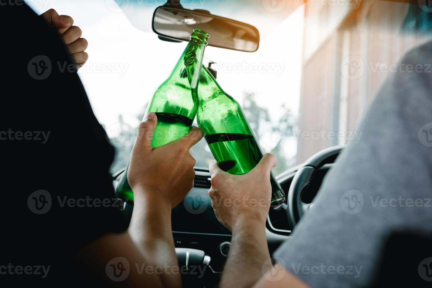dos amigos varones están celebrando en el auto mientras tocan una botella de cerveza juntos. foto